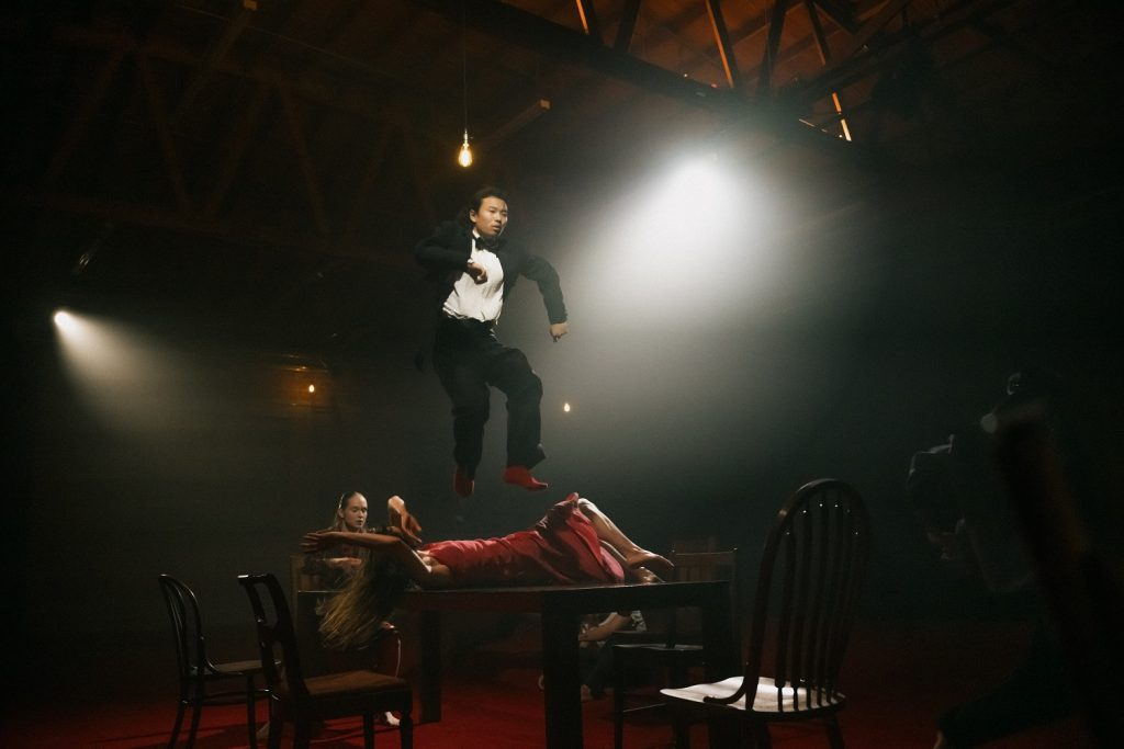 Courtney Conovan, Daphne Fernberger (on table) and Shu Kinouchi (in air) in The Missing Mountain by Bobbi Jene Smith and Or Schraiber - Photo by Josh S. Rose for L.A. Dance Project, 2023.